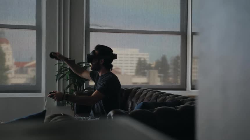 A man sitting on his couch using a vr headset raising and lowering his arms
