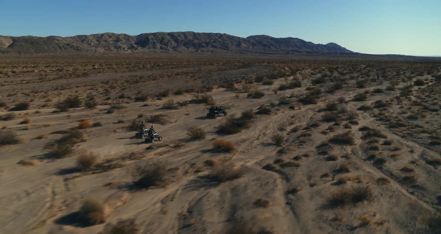People ride all terrain vehicles through the desert