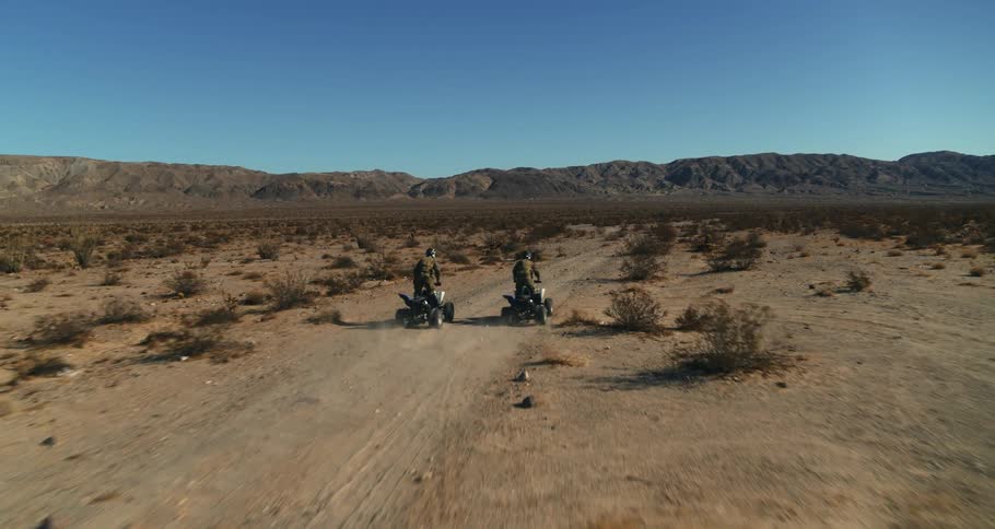 Two men ride all terrain vehicles through the dessert