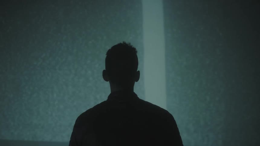 A man is facing a wall on which lights and images are being projected