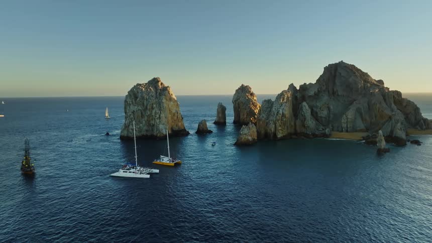 Sailing ships and sailboats float on ocean near rock outcroppings and small islands