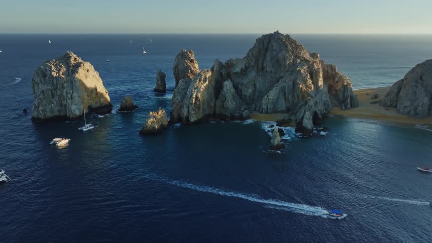 An aerial of a coastline with large rocks and boats traveling through
