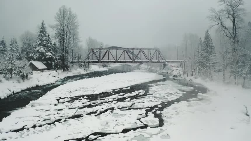A contrast between the harshness of winter and the urban landscape is revealed as we see a blanket of snow covering the ground under a bridge