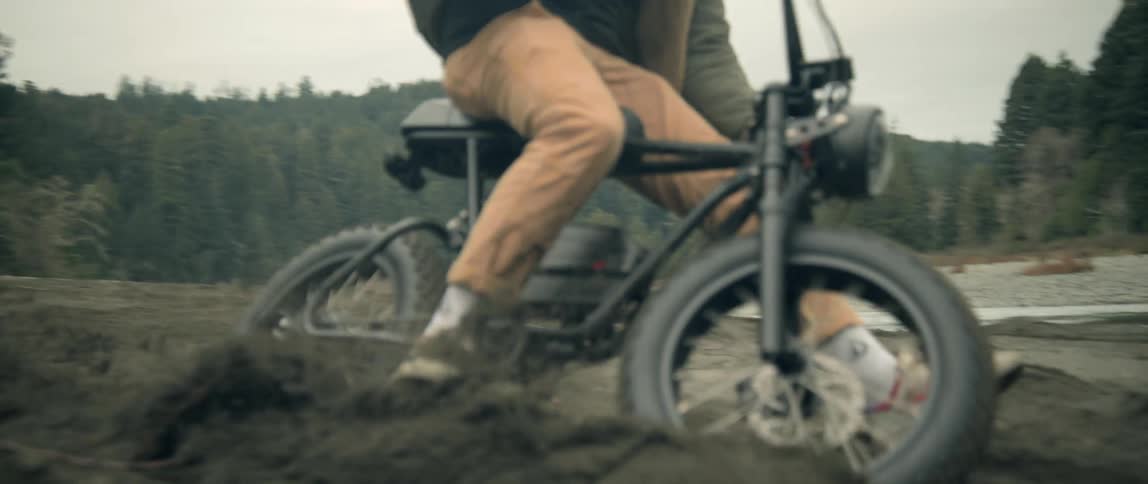 A teenage boy bikes through mud towards a river