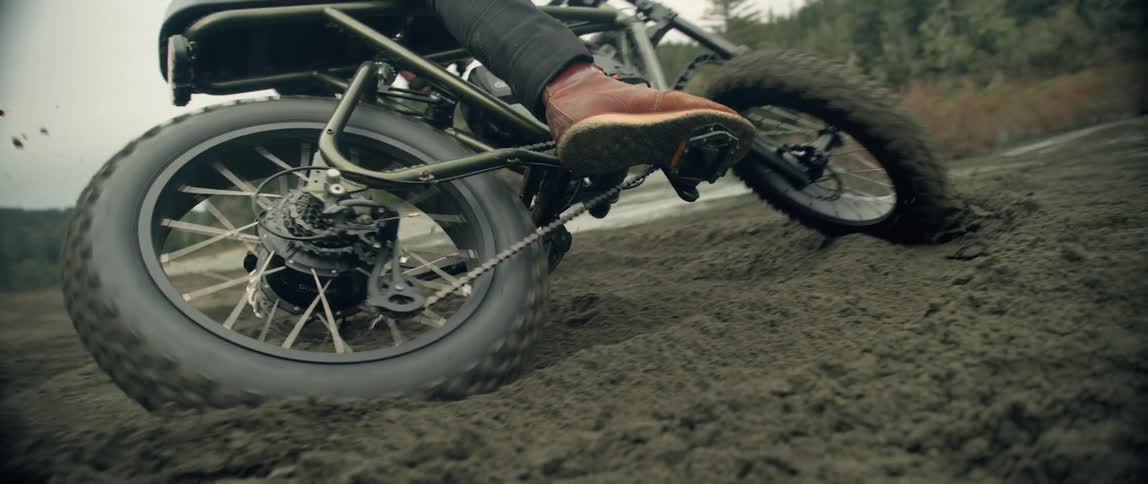 A person on a bike spins around in the mud in front of a river