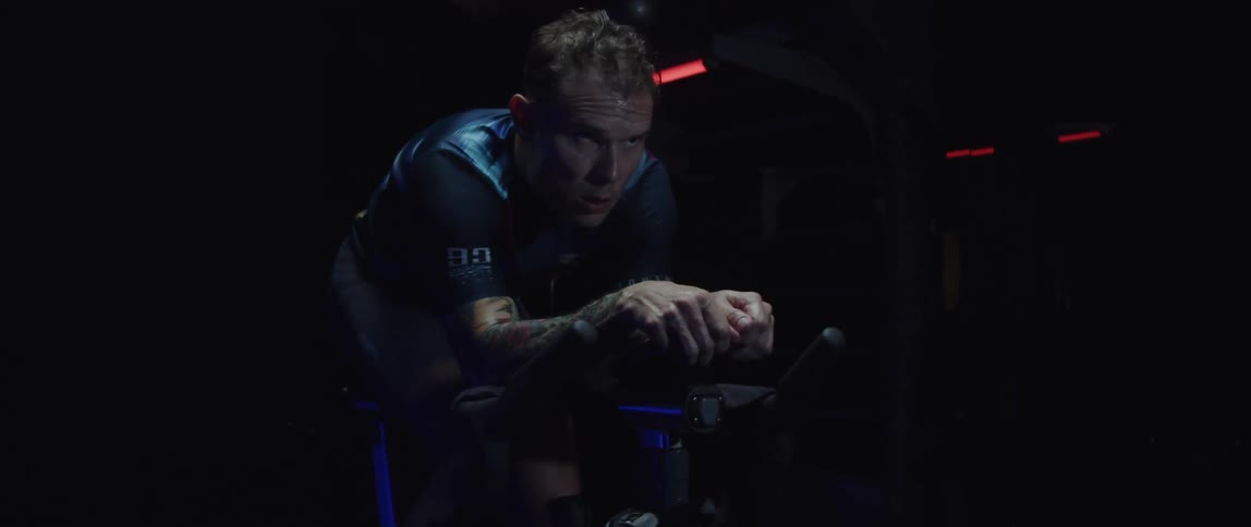 A man exercises on an exercise bike in a dark room