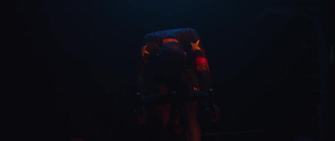 Focused man wearing a long sleeve shirt riding a stationary bike in a dark room