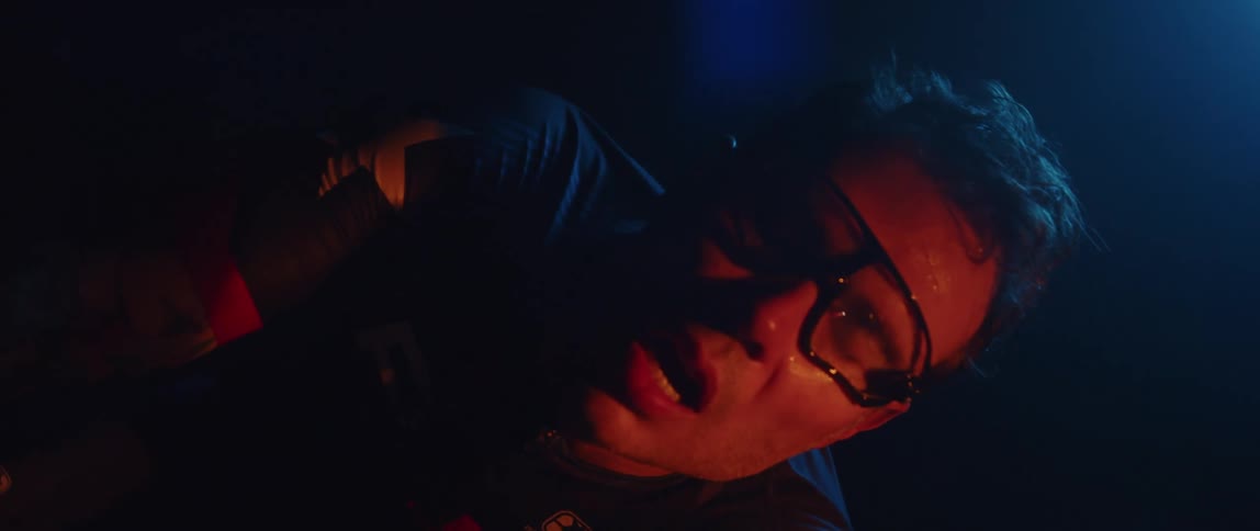 Male cyclist with glasses and jersey shirt breathes after riding exercise bike in dark room