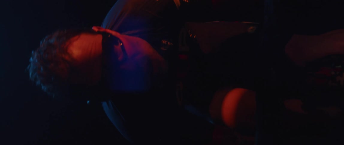 Twisting footage of a man pedaling on a static bicycle inside a dimly lit room against a dark background