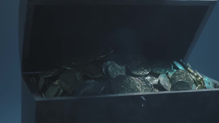 A hand opens a small chest filled with gold