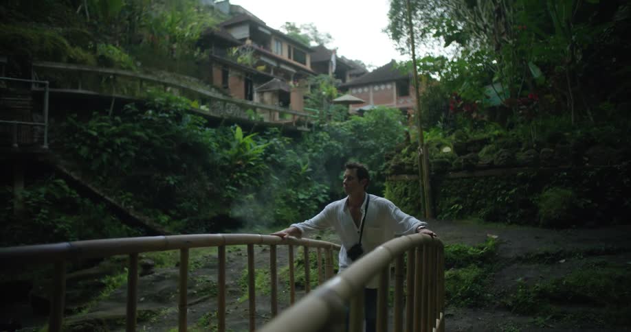 Man crosses a small bridge near a town on a rural area in the tropics