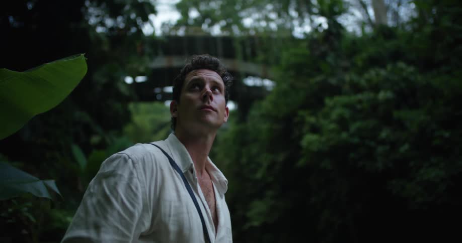 Young attractive man looking around near a bridge over a river on a tropical forest