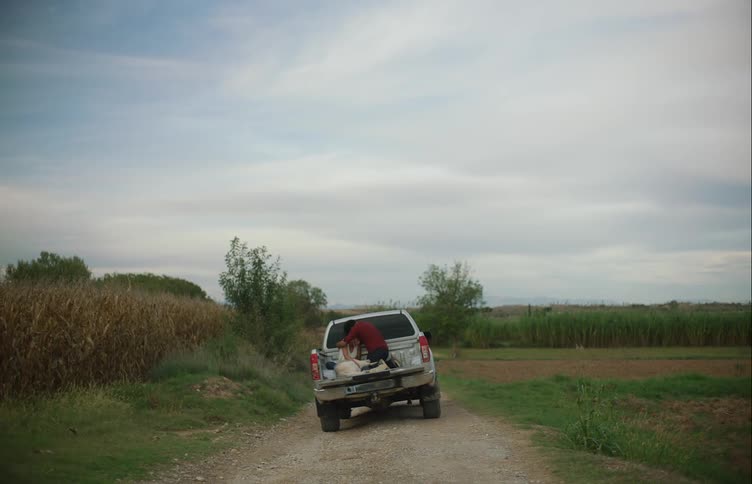 Man kneels next to woman in bed of truck parked on dirt road and comforts her as she cries