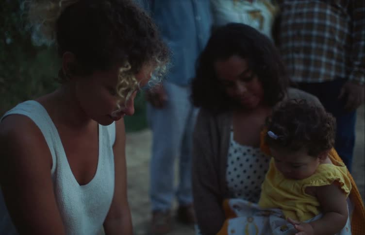 A woman hands something to a small baby being help by another woman