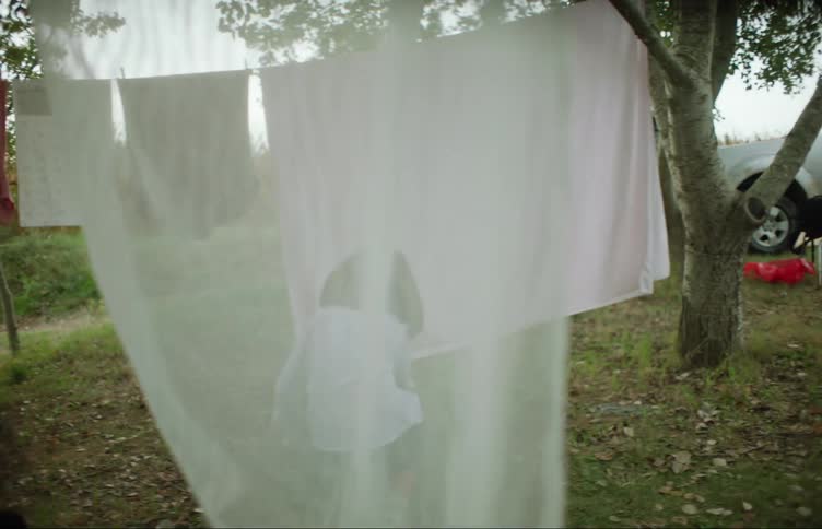 Girl moves around hanging laundry to crouch and comfort younger child