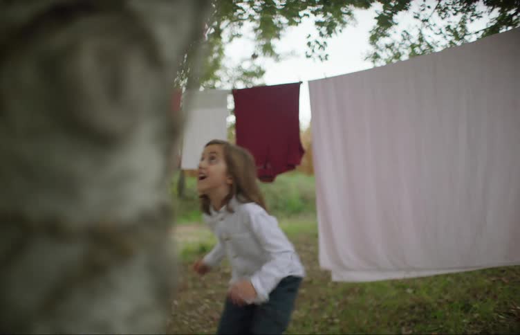 Girl playing with the clothes hanging on the backyard in the countryside