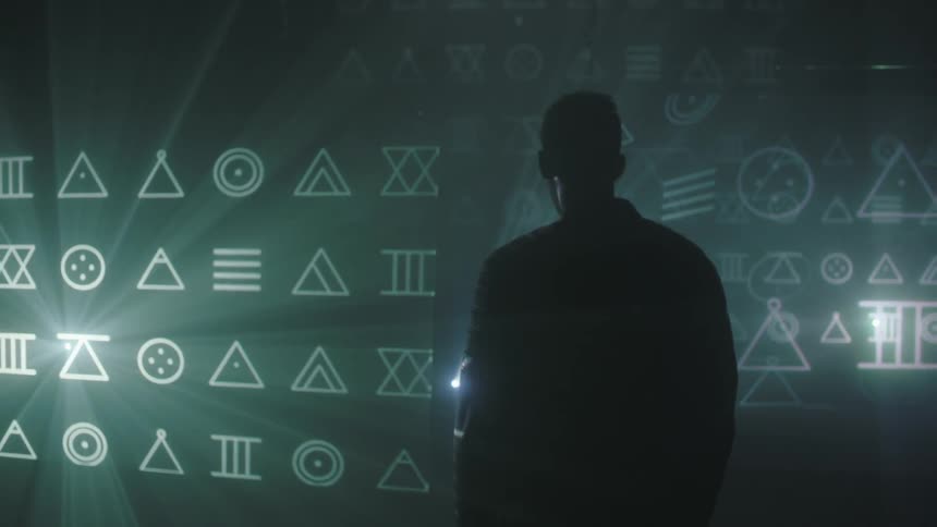 A man stands in front of a screen that is flashing symbols