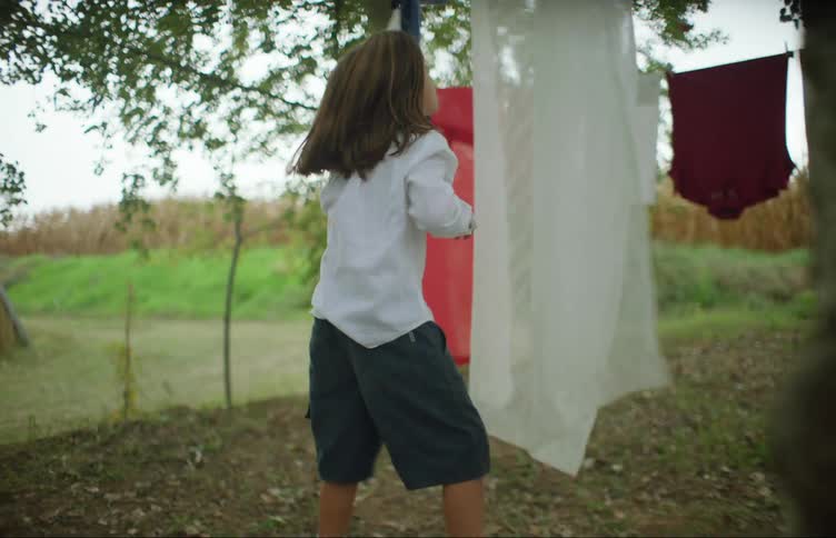 A young girl jumps at a sheet hanging on a laundry line outside