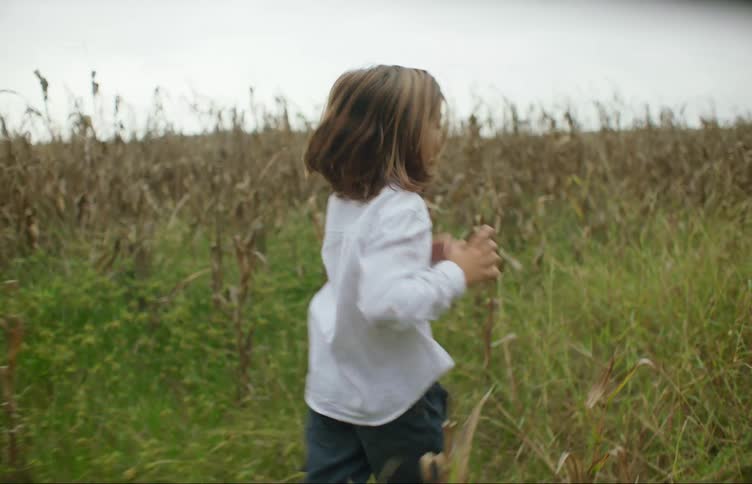 A child runs through a field of tall grass on a cloudy day