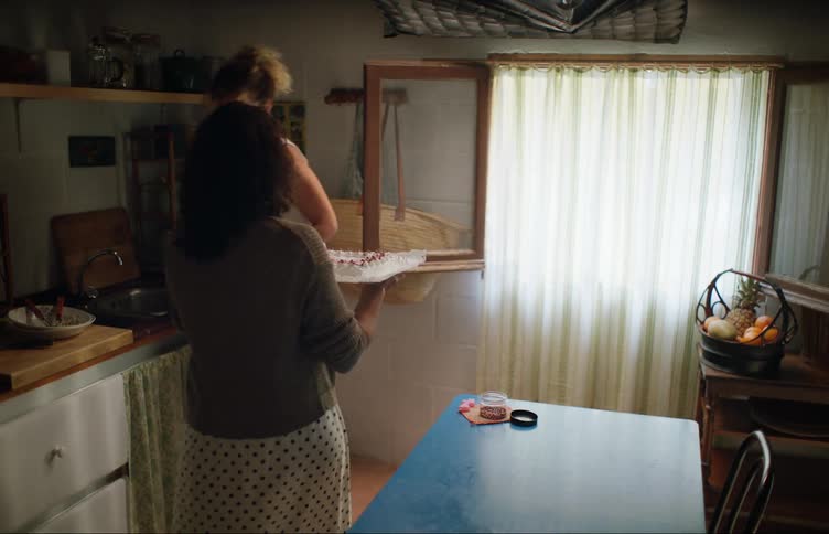 A woman decorates a cake and nearly collides with another woman while attempting to carry the cake out of the kitchen