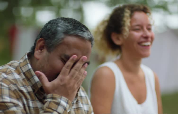 A man and woman laugh while chatting in their backyard