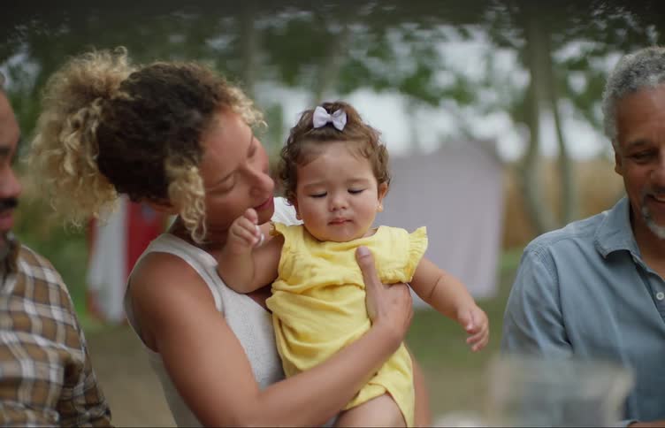 Woman sitting at the table on a family reunion in the backyard picks up a toddler in her arms
