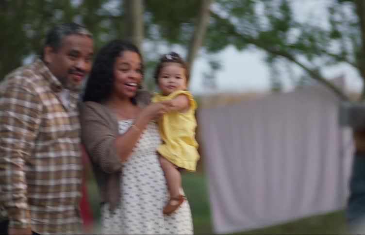 Young happy couple holding a baby gather in the backyard at evening