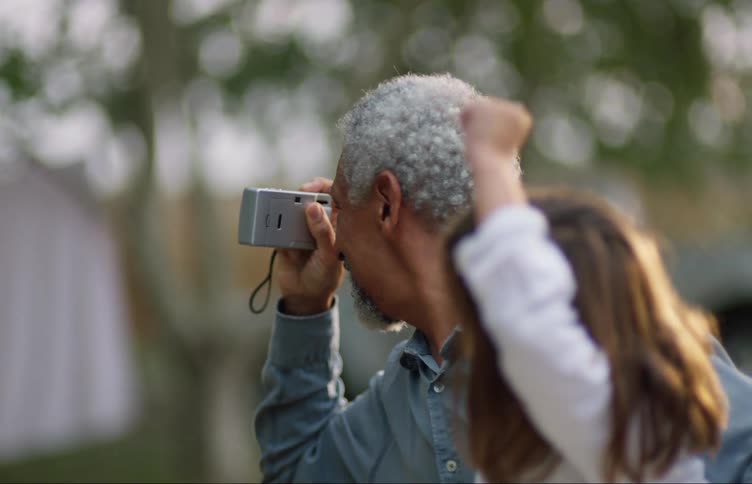 A man uses a camera to take a photograph while carrying a girl
