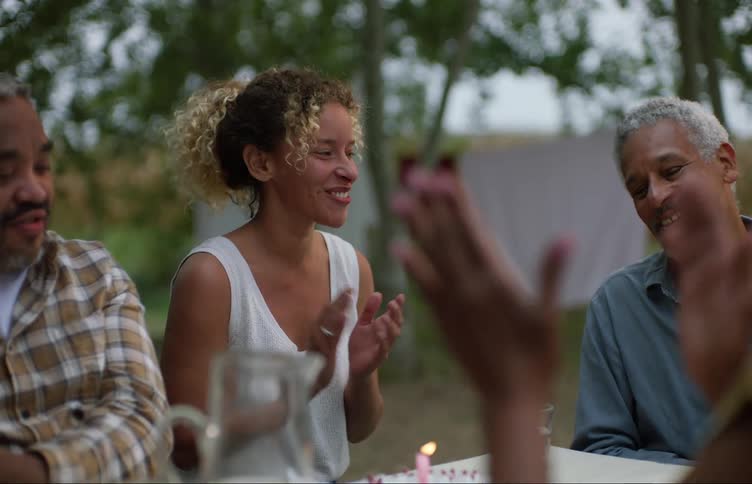 Family sings to man as birthday cake is place on table before one woman stands up and leaves