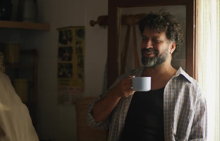 A man holding a coffee cup at home laughs and talks