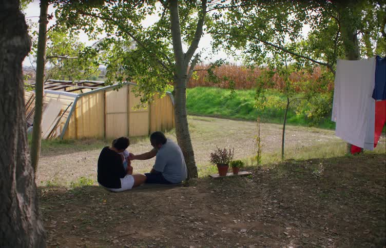 Family carrying a toddler leisurely sitting under a tree in the countryside