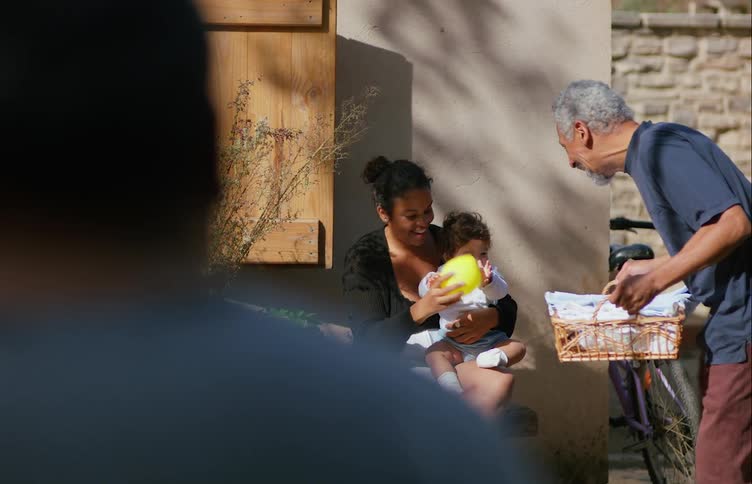 A woman plays with her son outside as a neighbor walks by with laundry