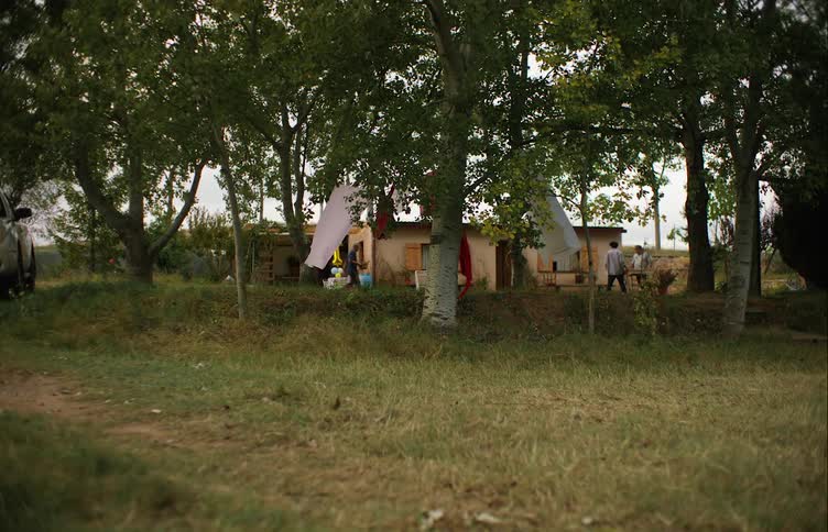 Two men carry table to backyard and another carries a bowl while laundry flaps on clotheslines