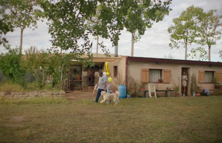 A man walks out of his house with his dog and moves through the yard
