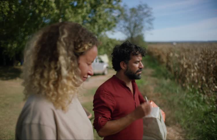 Man carrying wrapped gifts moves to stand near woman in ruralbackyard and offers her a cigarette