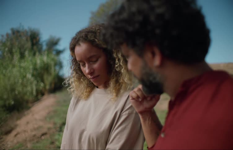 Man turns to look left then back at the woman standing to his right as they converse outdoors