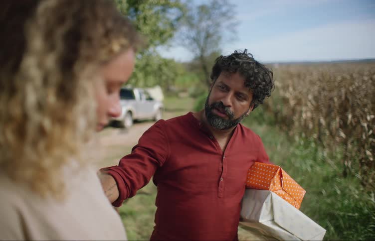 A man holding gifts hugs a woman standing in a rural area