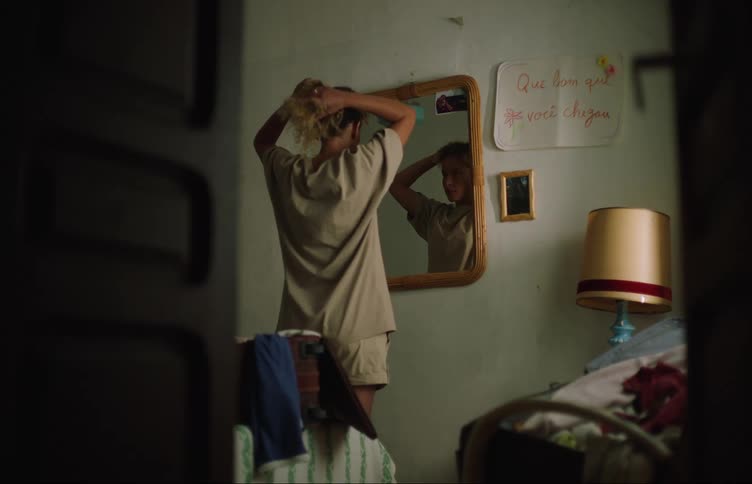 A woman stands in front of a small mirror and puts her hair in a ponytail