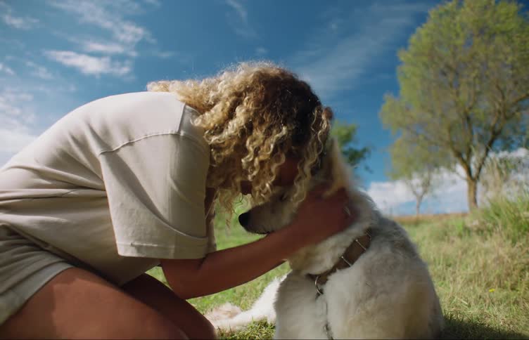 Woman with curly hair leans down to hug a white dog