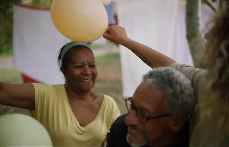 A man and woman laugh outside in their yard while their daughter puts a balloon on her mothers head
