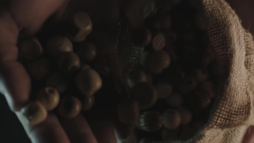 A man pours beads into a burlap sack