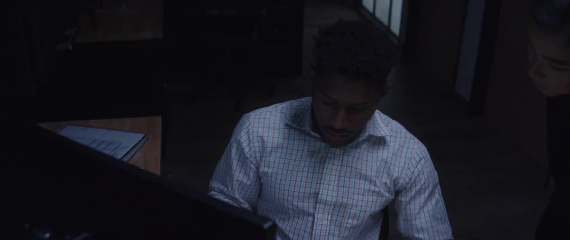A man in an office picks up a folder and shows it to a woman and then points at the computer in front of him