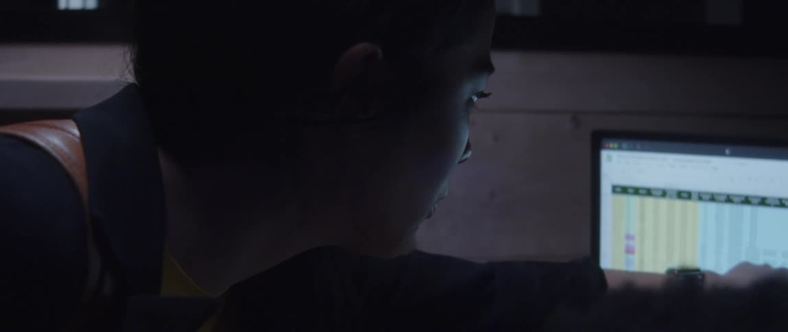 A woman reviewing a coworker's computer screen in a dark office space