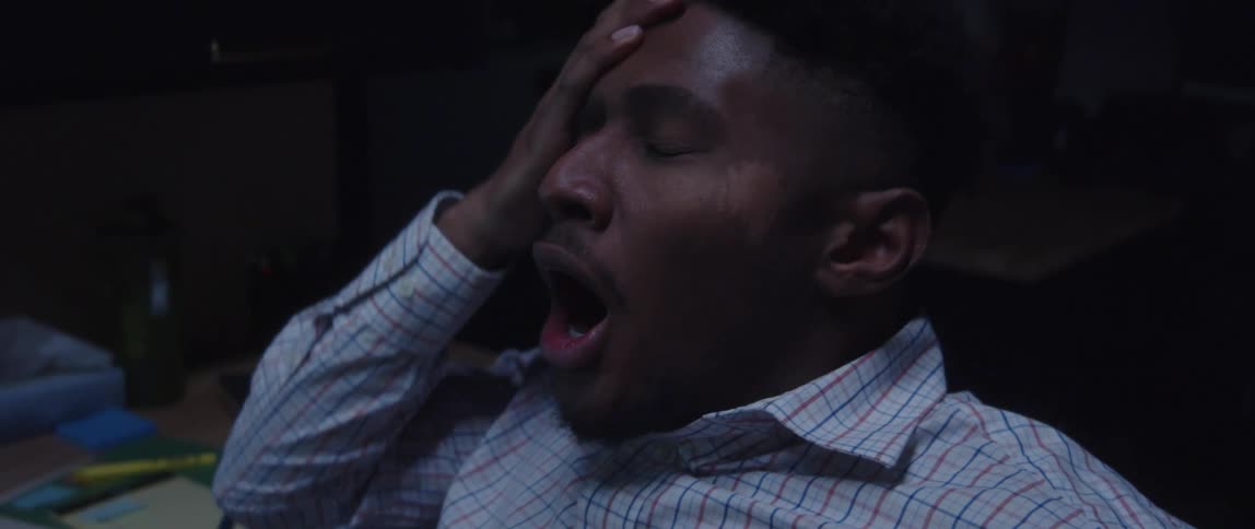 A man sitting rubbing his eyes and then yawning looking exhausted