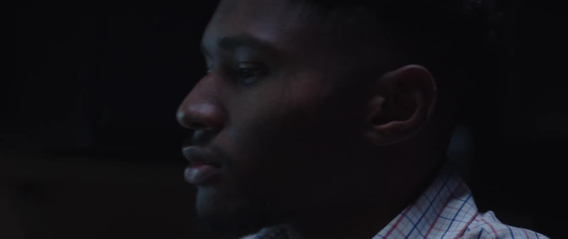 Black man in office at nighttime leaning forward to answer phone