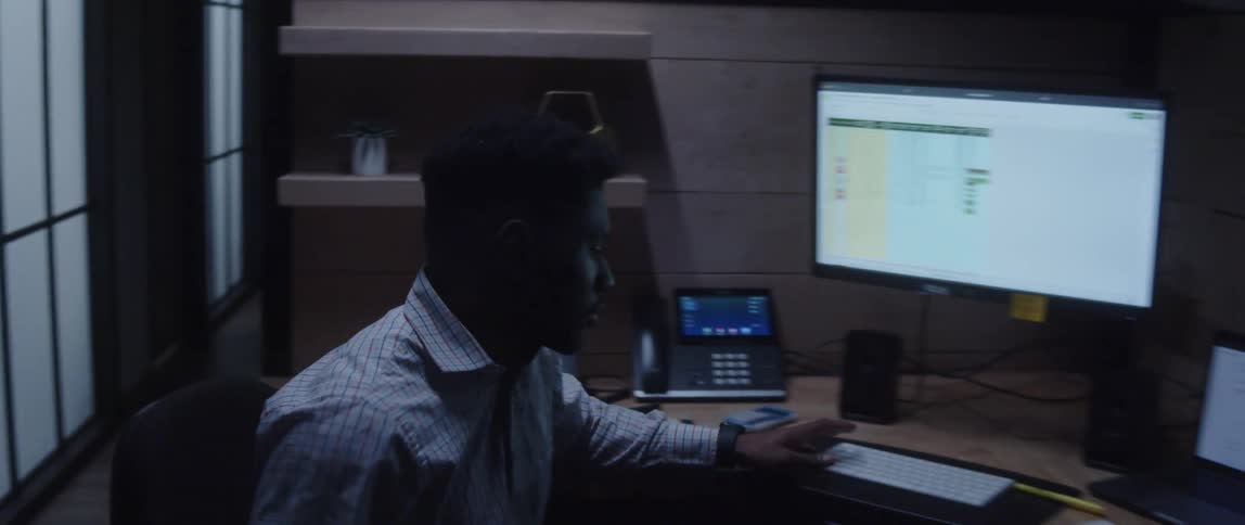 A young man sitting at an office desk is thinking about something then suddenly comes up with an idea and quickly moves his chair closer to the computer desk and starts typing on the keyboard