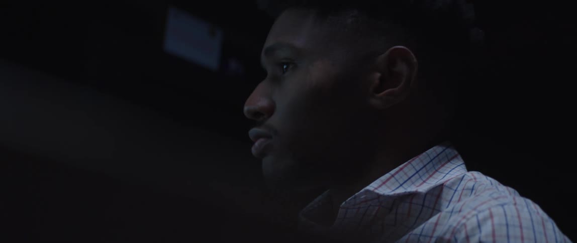 Light from a computer monitor shines on the face of a man sitting at a desk working