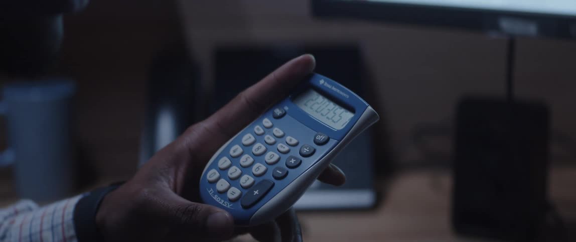 A man looks at the screen of a calculator while sitting at a desk