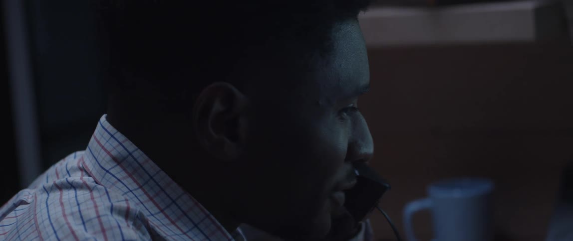 A man is sitting at a desk talking on the phone