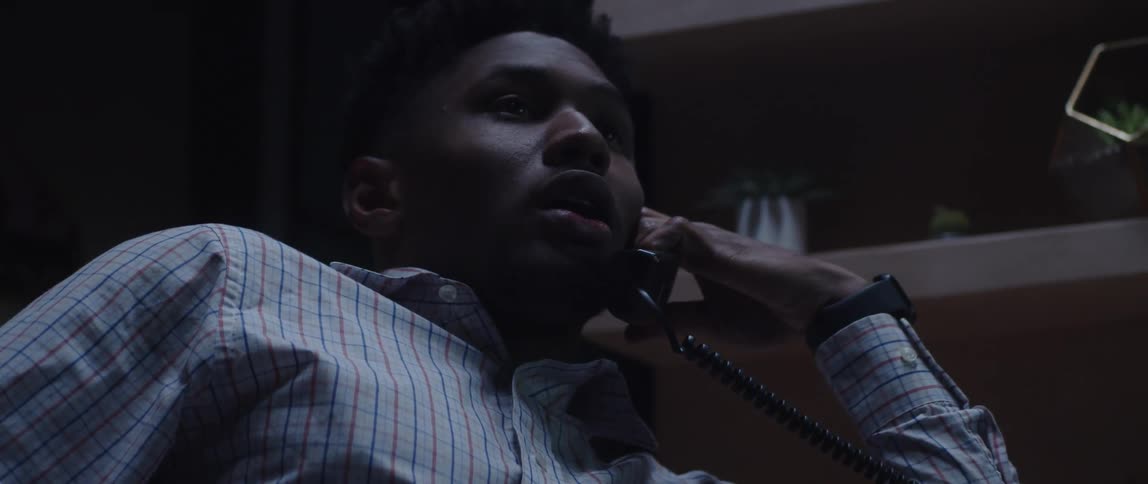 Man in office leans toward shelves while talking on the desk phone